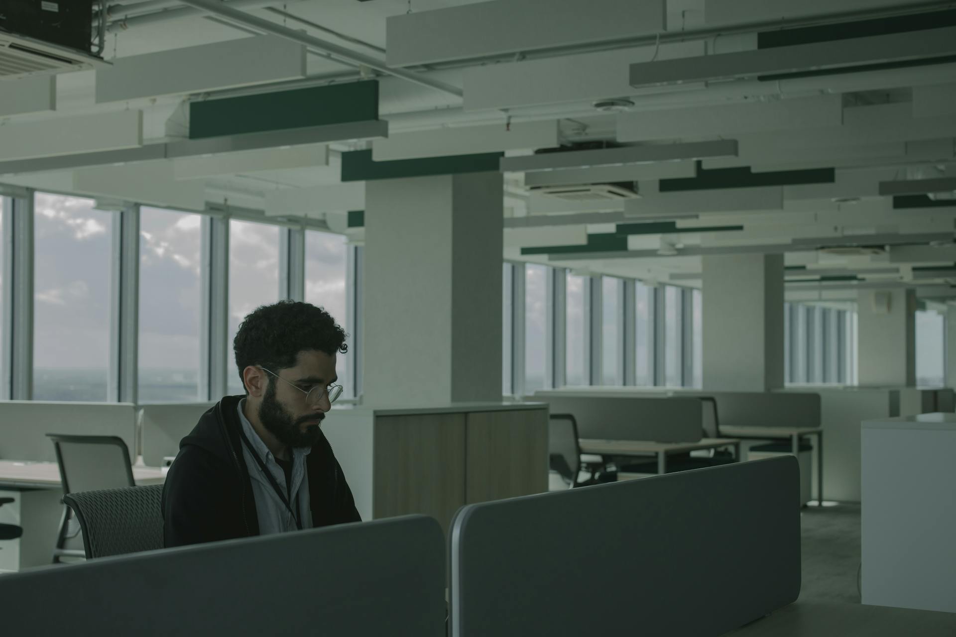 Man in black jacket sitting alone in a bright office, focused on work.
