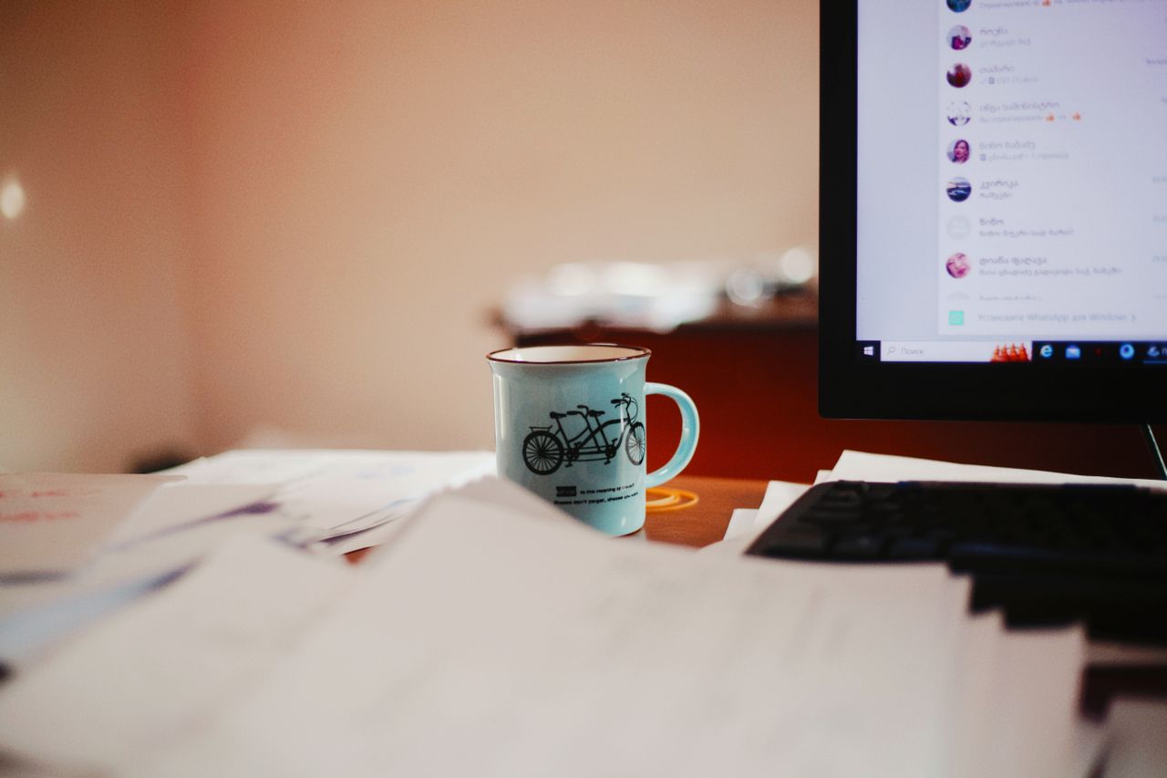 Person's focused workspace with a steaming coffee cup beside a desktop computer, representing the deep concentration and ritual needed to enter a flow state
