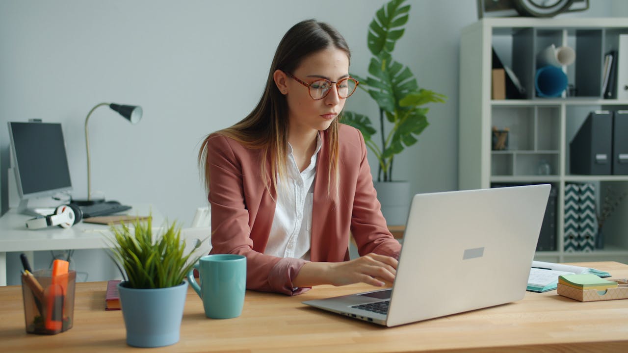A focused professional woman working at her desk with a laptop, illustrating the 80/20 rule by concentrating on high-impact tasks for maximum productivity.