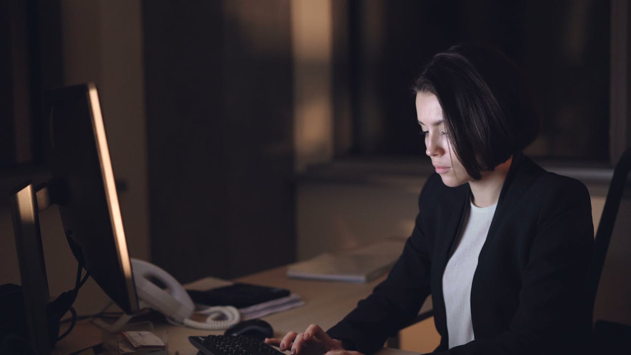 Woman working late at desk, deeply focused in a quiet office setting.