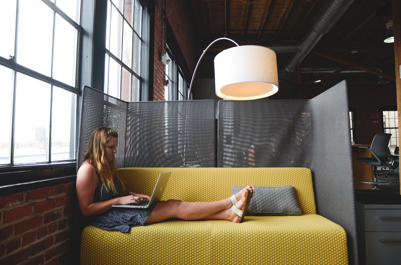 Woman working on her laptop while sitting comfortably on the sofa, representing the common 'I'll do it later' habit that quietly sabotages your day.