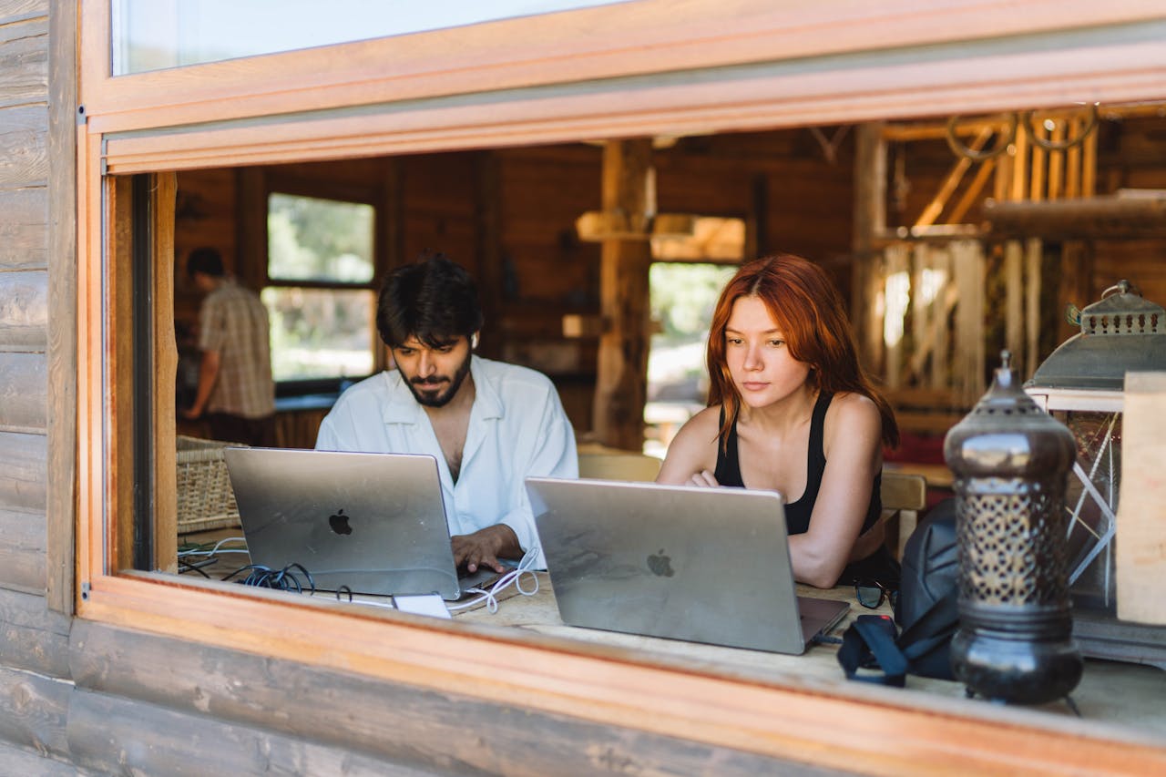 Remote professionals using MacBooks near large windows in a bright coworking space designed for productivity and collaboration.